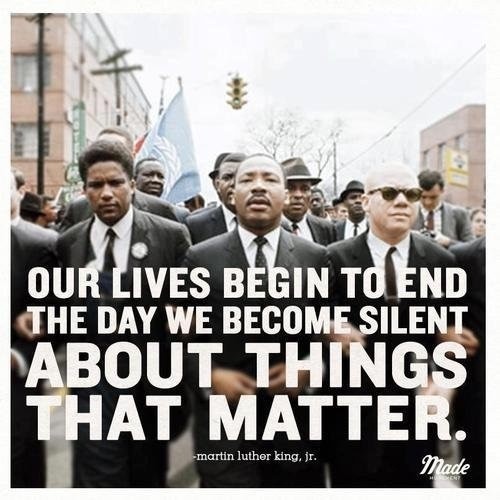 A group of men in suits march on a street, holding a banner. Text: "Our lives begin to end the day we become silent about things that matter." - Martin Luther King, Jr.