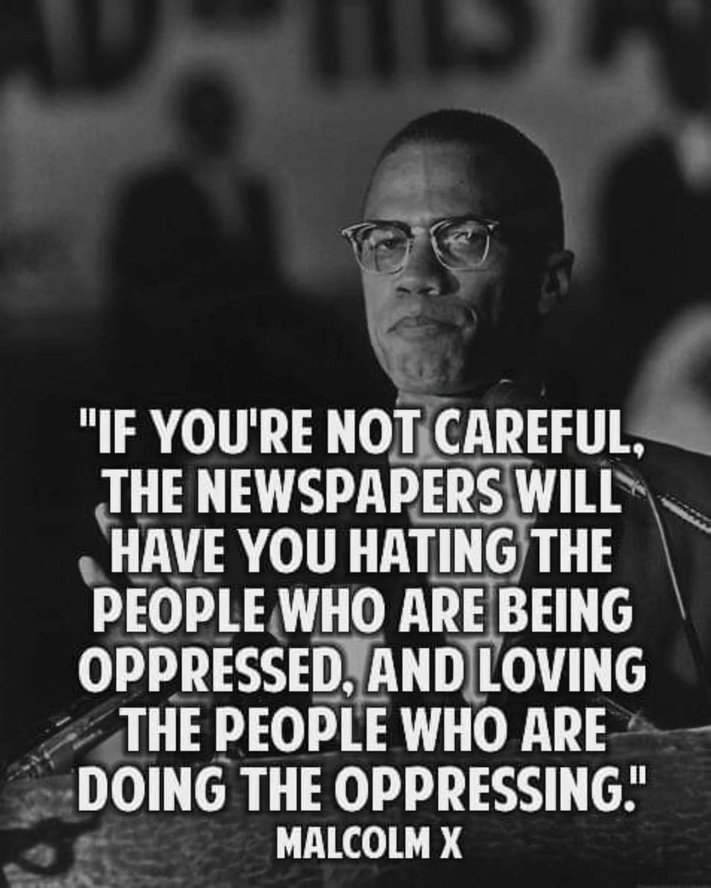 Alt text: Black-and-white photo of a man in glasses speaking at a microphone, shown from the chest up. The background is blurred, keeping focus on his serious expression. Over the image is a bold, white text quote that reads: “If you’re not careful, the newspapers will have you hating the people who are being oppressed, and loving the people who are doing the oppressing.” At the bottom, the quote is attributed to Malcolm X.